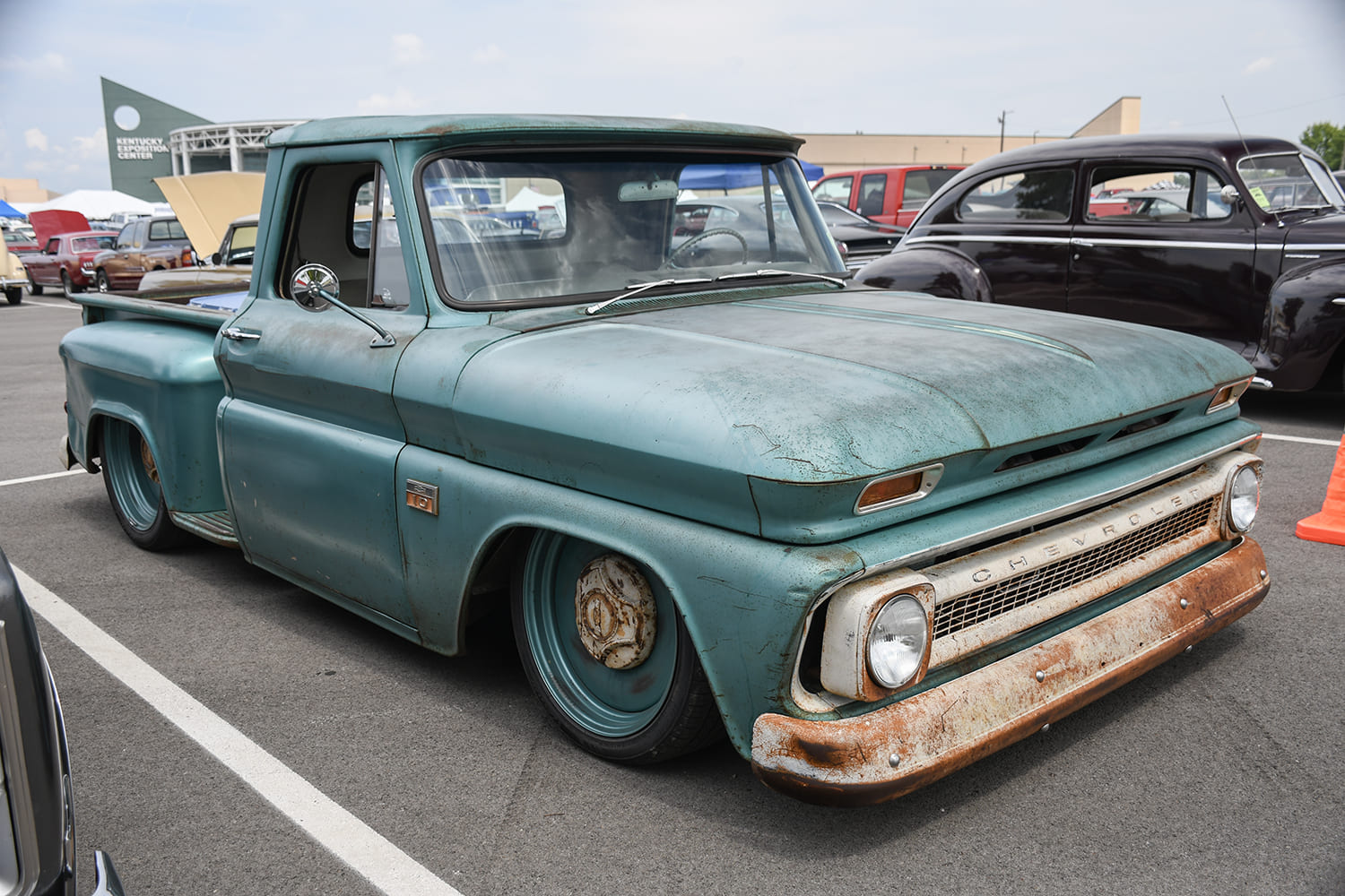 Low front three-quarter view of a heavily weathered turquoise-green Chevrolet C10 pickup with a white roof and faded bumper laid out on the asphalt.