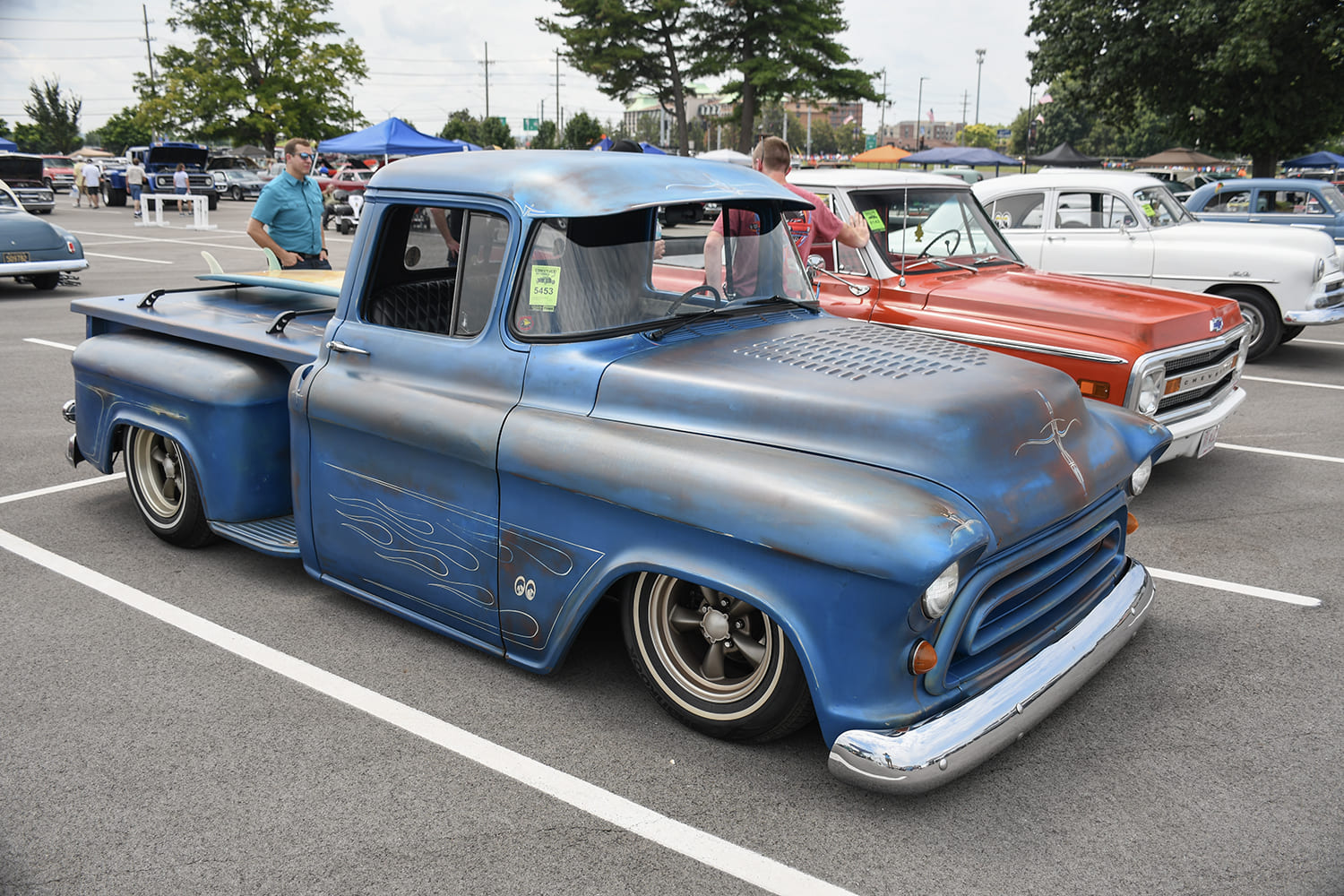 Front three-quarter shot of a lowered matte blue and primer Chevrolet Task Force pickup featuring custom ghost flames, cab sun visor, and whitewall tires.