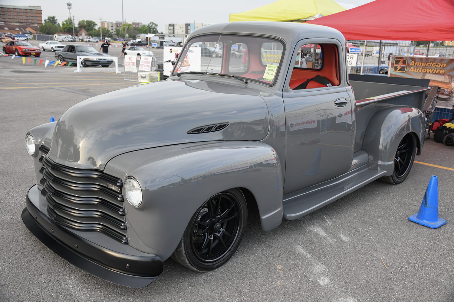 Front three-quarter angle of a glossy battleship gray Chevrolet 3100 pickup truck with black front grille and black wheels parked in an outdoor show lot.