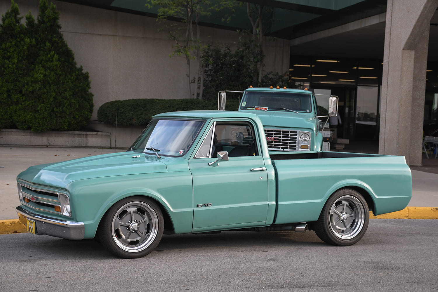 Driver-side profile of a lowered light seafoam-green Chevrolet C10 fleetside pickup featuring side-exit exhaust tips and gray five-spoke alloy wheels.