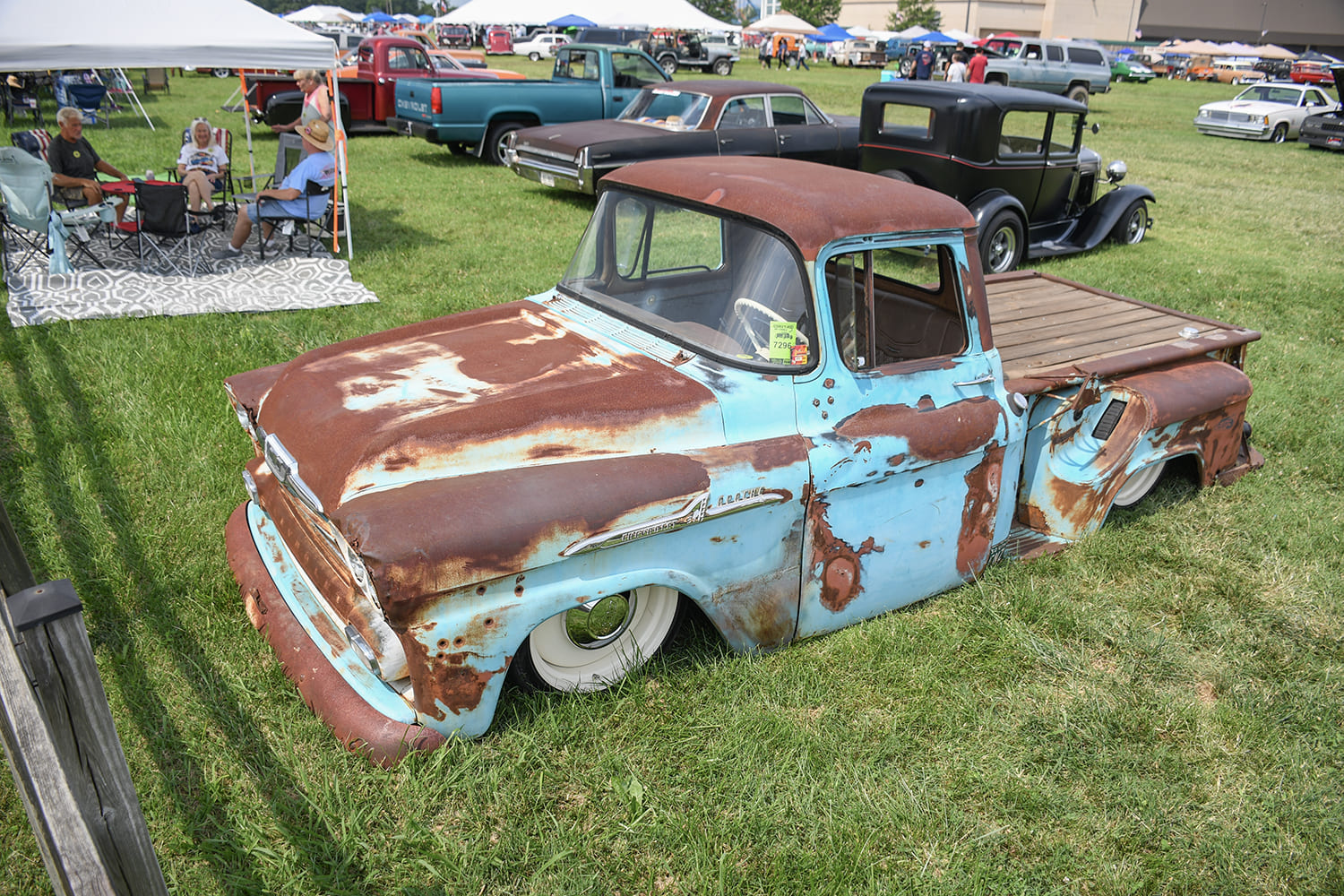 High overhead three-quarter view of a heavily weathered patina light blue and rust Chevrolet Apache pickup laid out flat on a grassy lawn with whitewall tires.