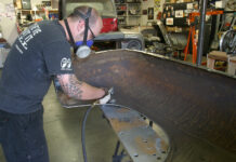 KBS Coatings Ultimate Rust Solution Mechanic wearing a respirator using an angle die grinder with an abrasive disc to clean rust off an automotive inner fender.
