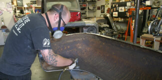 Mechanic wearing a respirator using an angle die grinder with an abrasive disc to clean rust off an automotive inner fender.