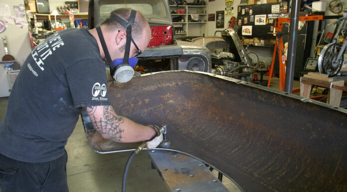 Mechanic wearing a respirator using an angle die grinder with an abrasive disc to clean rust off an automotive inner fender.