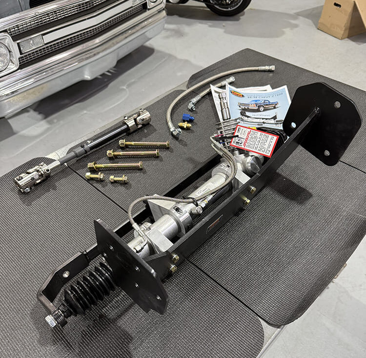 Unboxed Flaming River rack and pinion conversion kit laid out on a table, showing the mounting cradle, steering shaft, hardware, and installation instructions for an OBS Chevy truck.