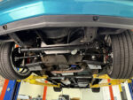 Underside view of an OBS Chevy truck on a lift showing an installed Flaming River rack-and-pinion steering conversion kit with tubular control arms and aftermarket suspension.