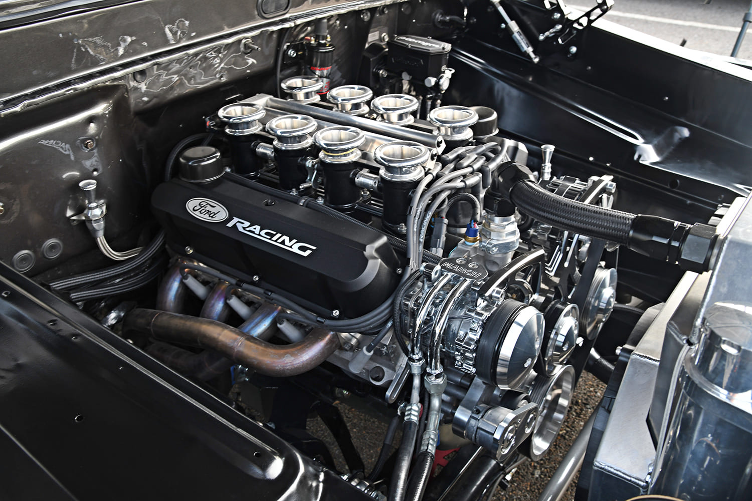 Detailed engine compartment view of a Ford Racing V8 featuring individual throttle body velocity stacks, March serpentine drive, and aluminum radiator.
