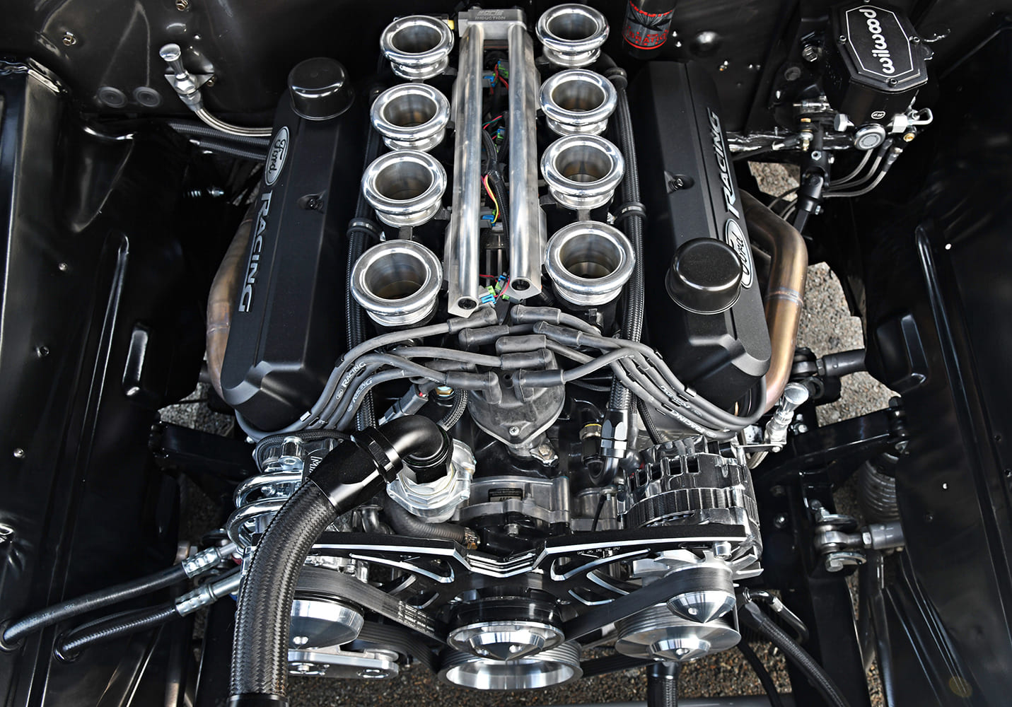Top-down macro view of an eight-stack EFI system with polished trumpets, Ford Racing valve covers, and a Wilwood master cylinder in a clean shaved bay.
