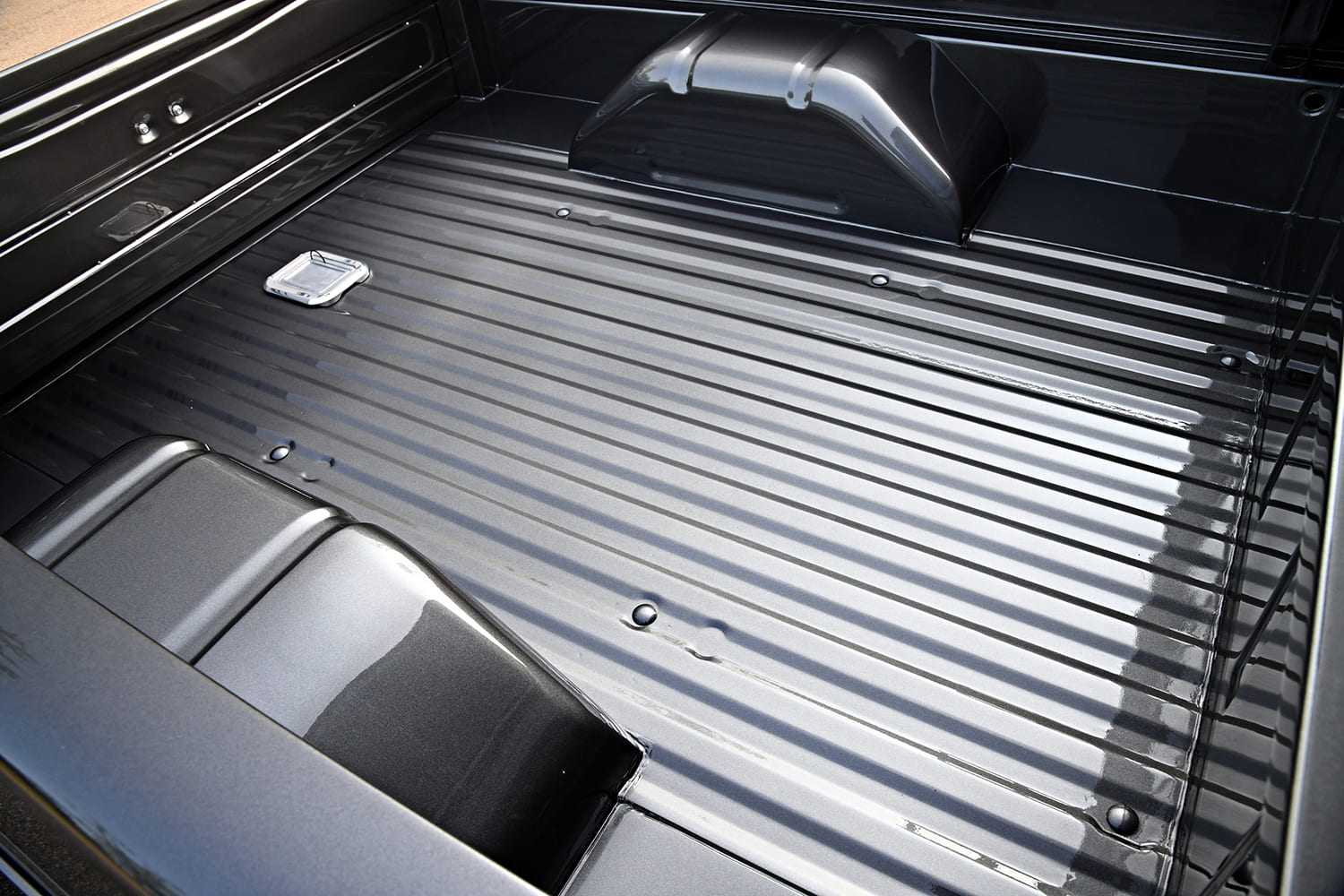 Overhead look into the painted gray metal bed of a custom 1972 Ford F-100 showing widened rear wheel tubs and a flush-mounted aluminum fuel door.