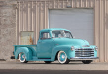 Front three-quarter view of a custom lowered 1953 Chevrolet 3100 pickup truck painted seafoam turquoise with whitewall tires and chrome grille parked outside a garage.