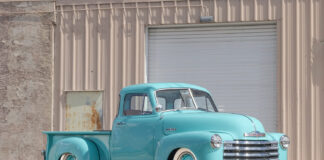 Front three-quarter view of a custom lowered 1953 Chevrolet 3100 pickup truck painted seafoam turquoise with whitewall tires and chrome grille parked outside a garage.