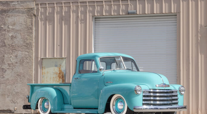Front three-quarter view of a custom lowered 1953 Chevrolet 3100 pickup truck painted seafoam turquoise with whitewall tires and chrome grille parked outside a garage.