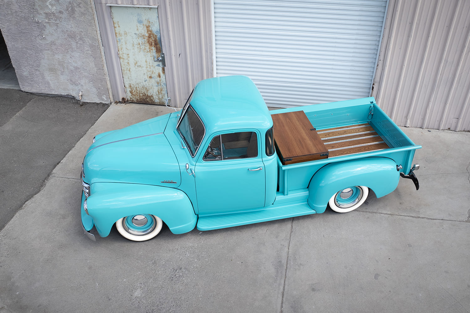 High-angle elevated view of a turquoise 1953 Chevy 3100 truck showing the custom finished wood-plank bed and storage chest.