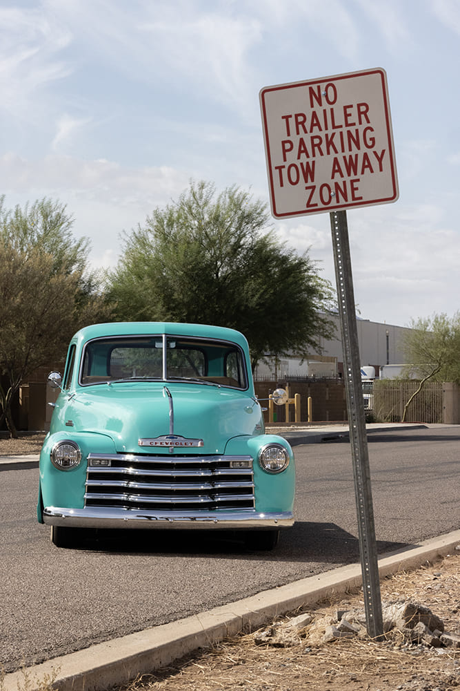 Front view of a vintage turquoise 1953 Chevy pickup parked at the curb next to a No Trailer Parking sign.