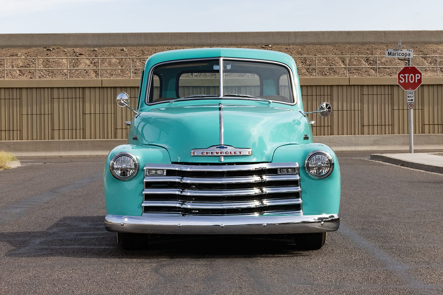 Direct head-on shot of the chrome five-bar grille, headlights, and bumper of a turquoise 1953 Chevrolet 3100 pickup truck.