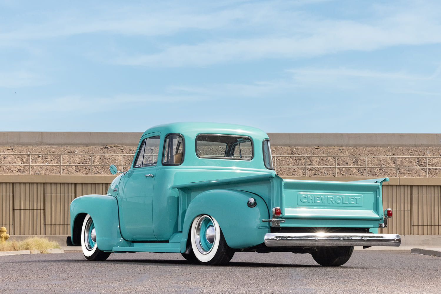 Rear three-quarter view showing the embossed Chevrolet tailgate, chrome bumper, and stepside bed of a turquoise 1953 Chevy truck.