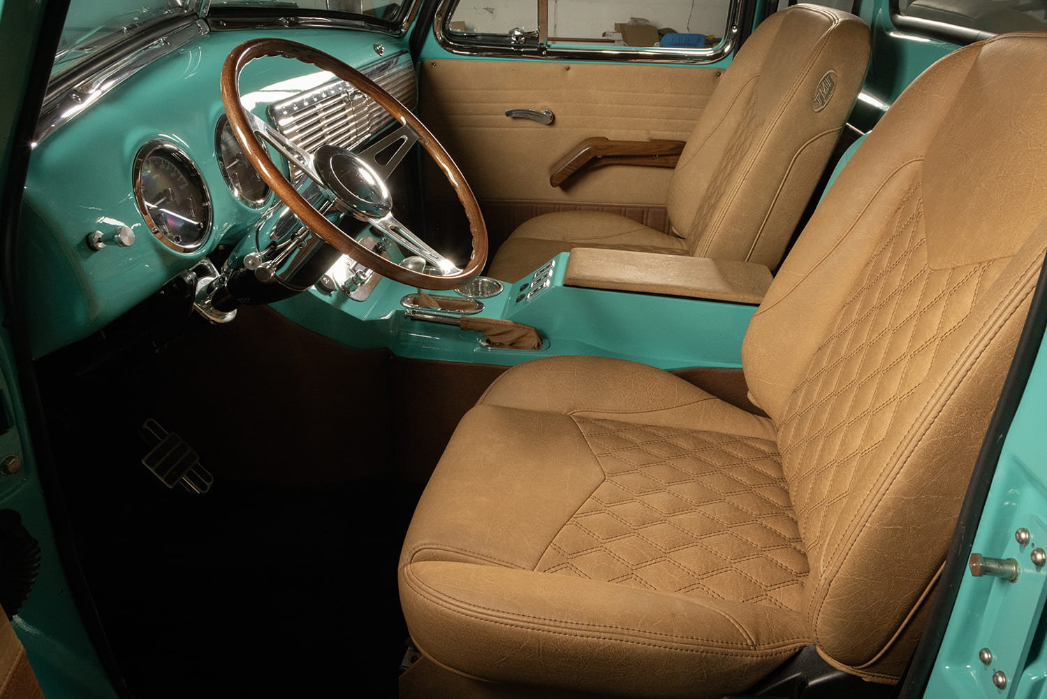 Custom cab interior of a 1953 Chevy truck featuring diamond-stitched tan leather bucket seats, matching center console, and wood steering wheel.