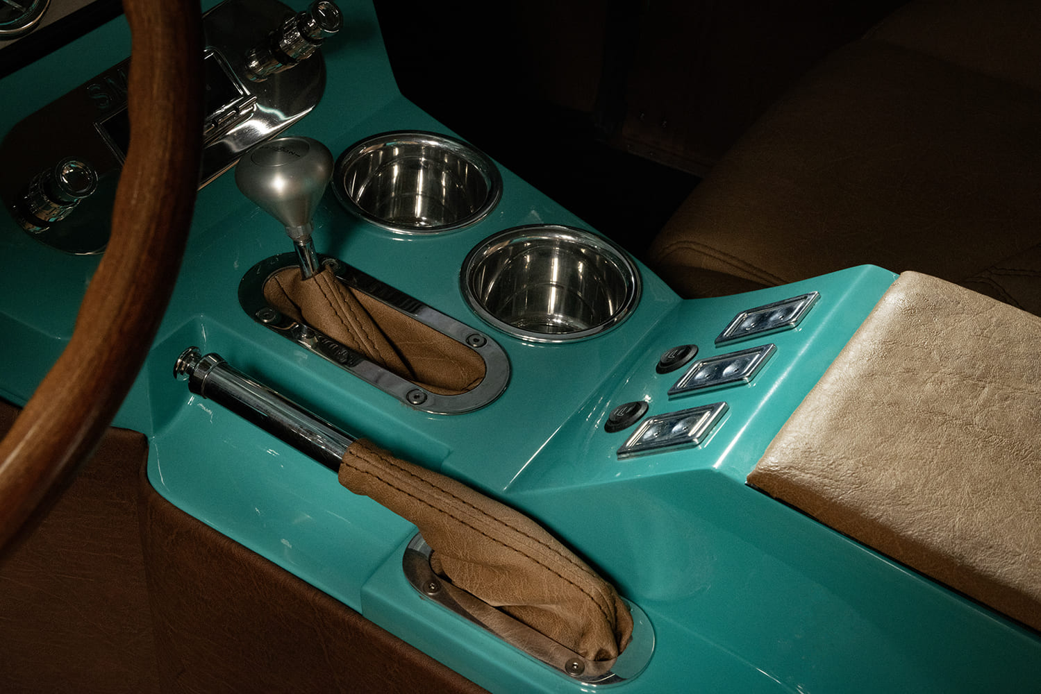 Center console detail in a 1953 Chevy truck showing an automatic floor shifter, dual polished cup holders, power window switches, and tan leather armrest.