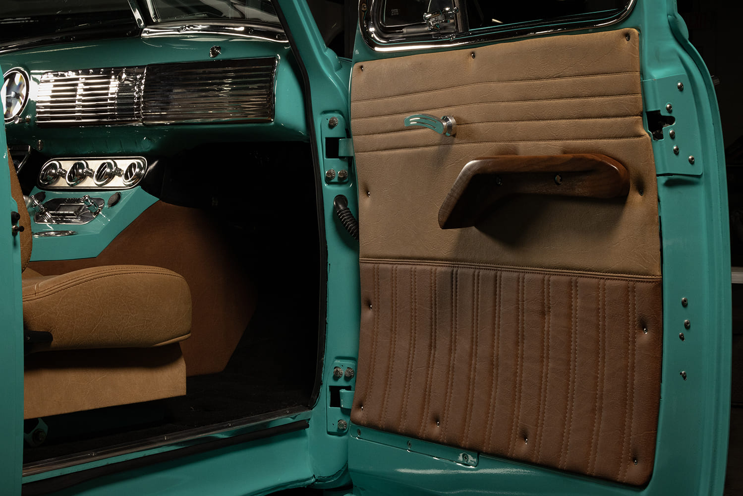 Open truck door revealing custom two-tone tan pleated leather upholstery, sculpted wood armrest, and turquoise painted frame.