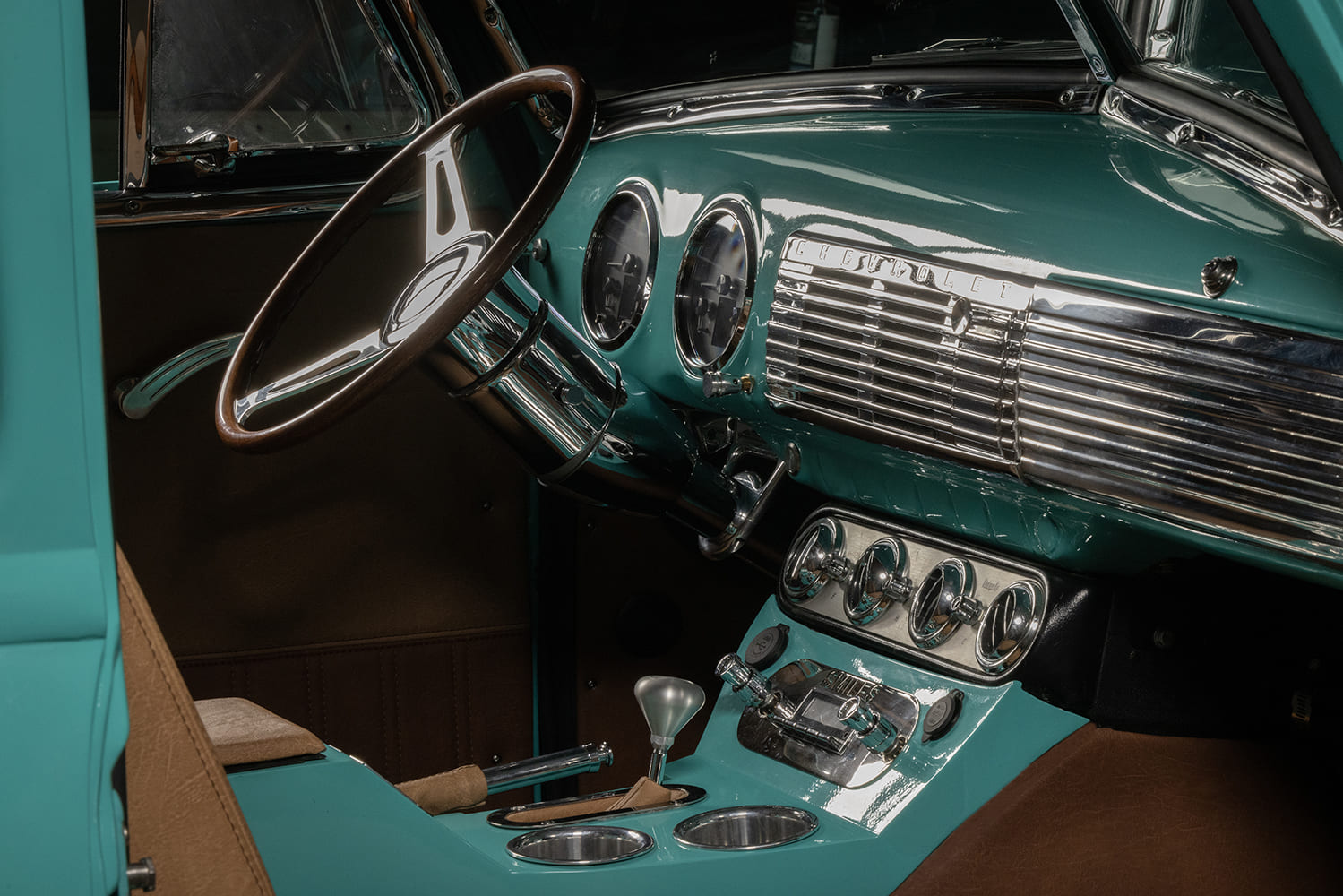 Angled view of a turquoise painted dash in a 1953 Chevy truck featuring a polished tilt steering column, wood steering wheel, and chrome speaker grille.
