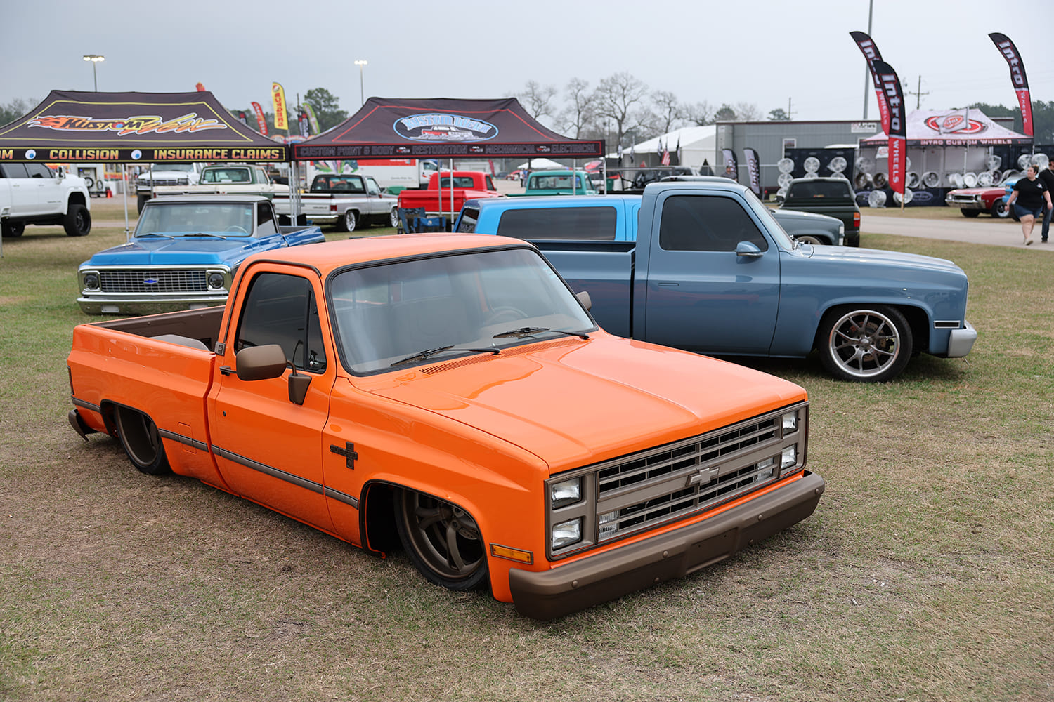 Front three-quarter view of a bright orange bagged squarebody Chevrolet C10 pickup laid out on the grass at Lone Star Throwdown.