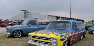 Front three-quarter angle of a customized blue squarebody Chevrolet Suburban featuring airbrushed yellow and orange flames laid out on the grass.