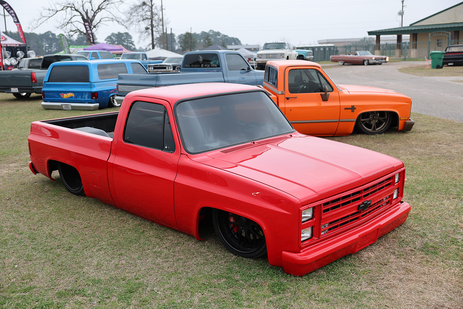 High front three-quarter view of a monochromatic bright red squarebody Chevrolet C10 pickup resting on the grass at an outdoor truck meet.