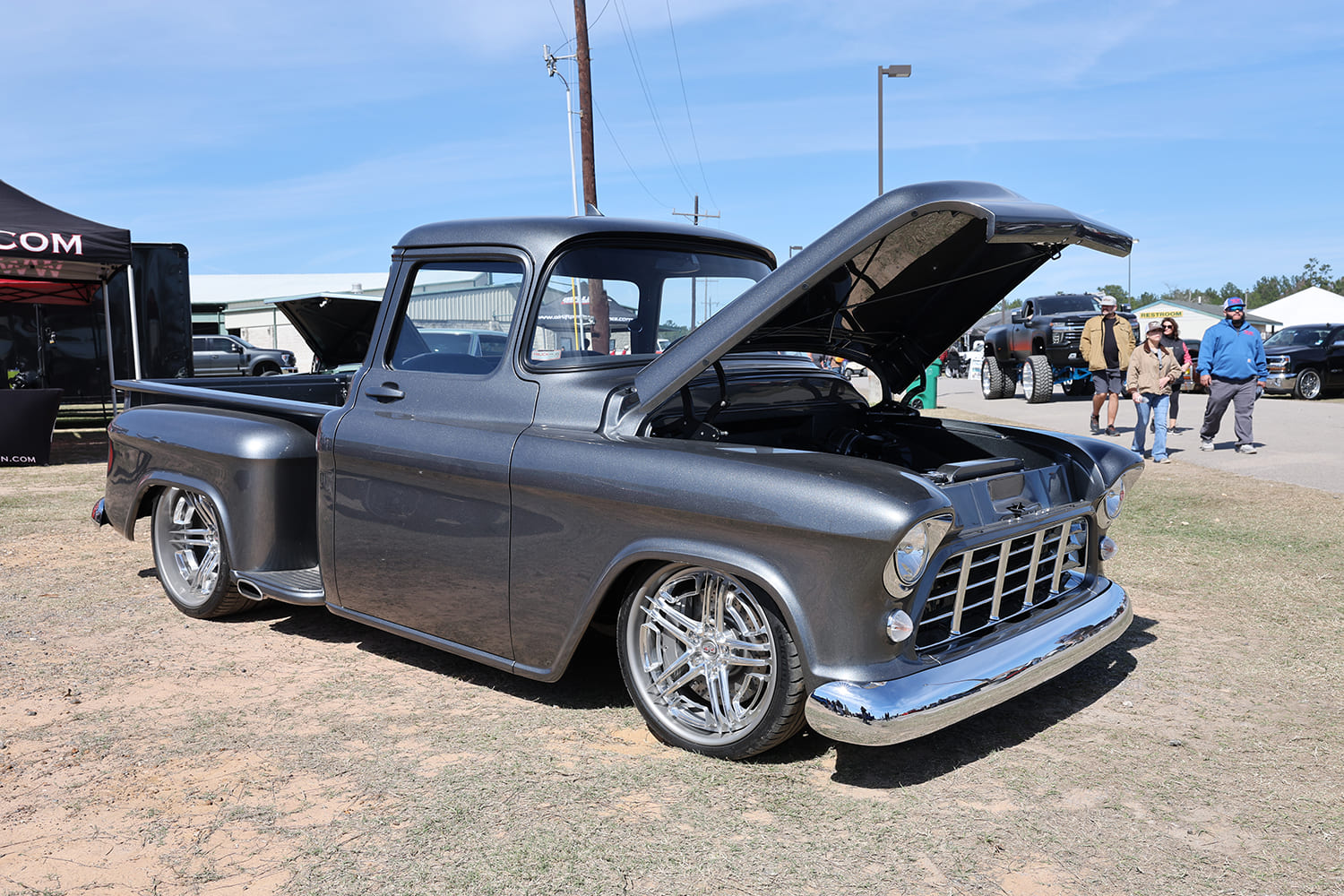 Front three-quarter angle of a metallic charcoal gray classic Chevrolet Task Force pickup with an open forward hood and chrome wheels on display.