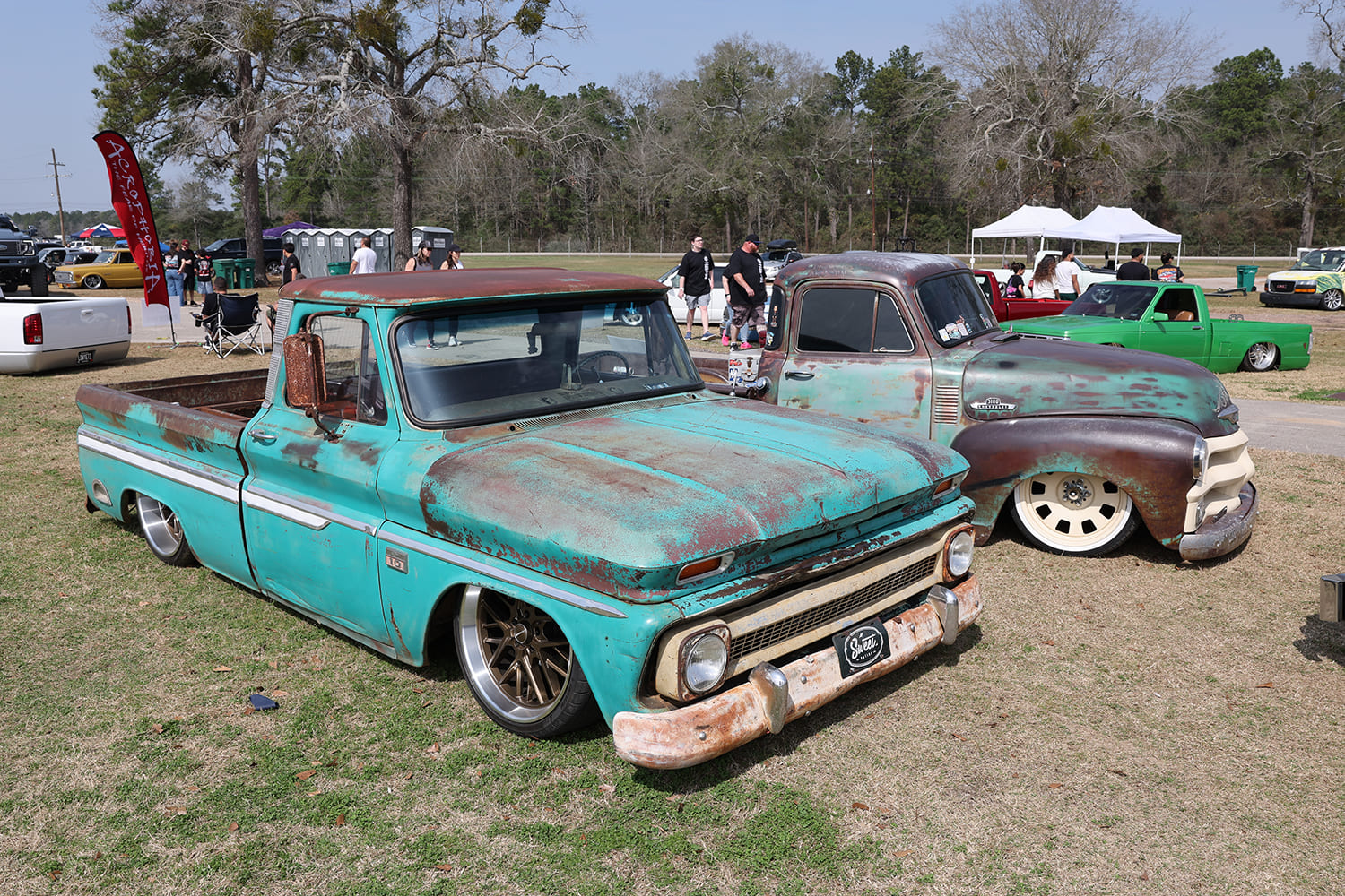 Front three-quarter shot of a lowered turquoise patina 1960s Chevrolet C10 parked next to a rustic brown classic Chevy pickup on the grass.