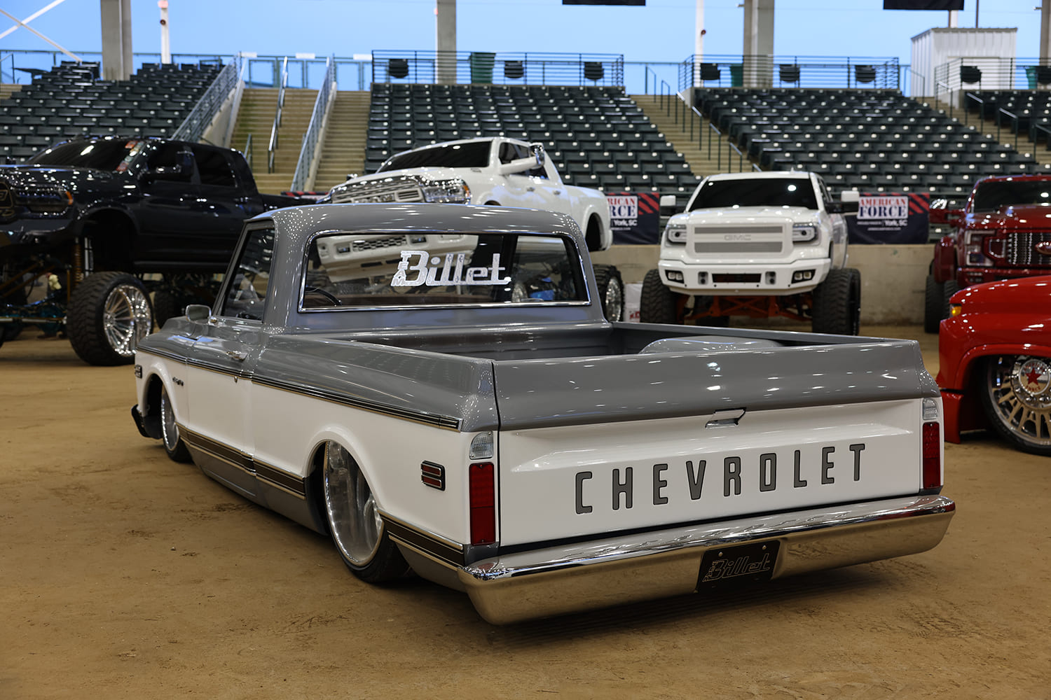Rear three-quarter view of a lowered two-tone gray and white Chevy C10 pickup displaying bold tailgate lettering and polished wheels.