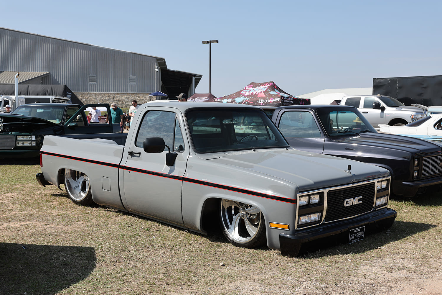 Front three-quarter view of a lowered gloss battleship gray GMC squarebody pickup truck featuring red pinstriping and polished deep-dish directional wheels.