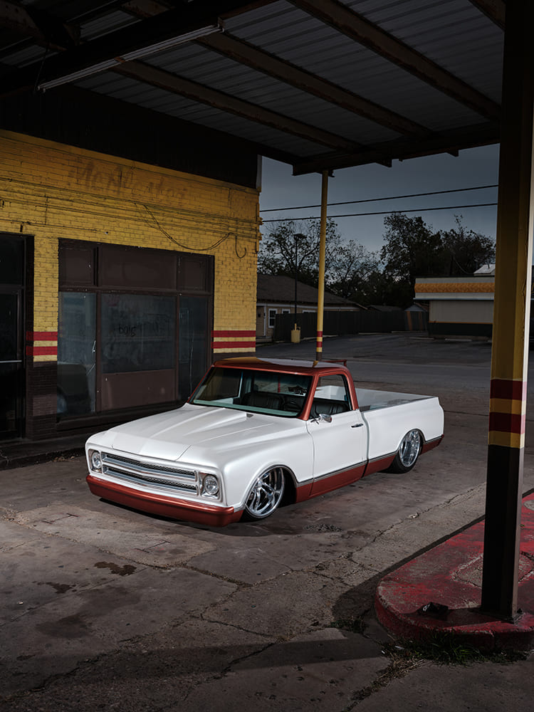 Elevated wide-angle view of a slammed pearl white and copper 1968 Chevy C10 resting under the canopy of an old gas station at twilight.