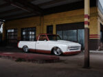 Low-angle front three-quarter perspective of a custom 1968 Chevy C10 pickup laid out on polished wheels in front of a weathered yellow brick building.