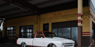 Low-angle front three-quarter perspective of a custom 1968 Chevy C10 pickup laid out on polished wheels in front of a weathered yellow brick building.