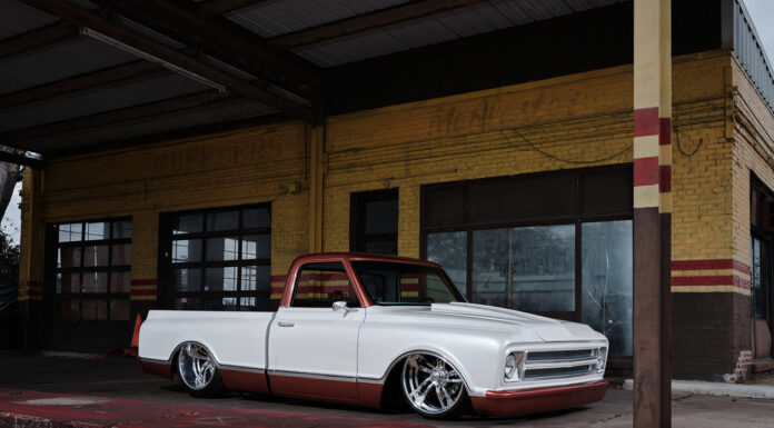 Low-angle front three-quarter perspective of a custom 1968 Chevy C10 pickup laid out on polished wheels in front of a weathered yellow brick building.