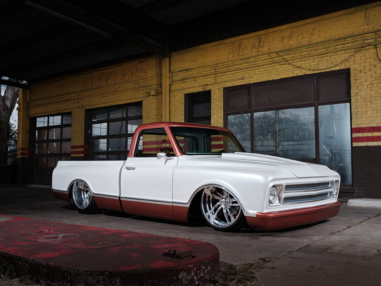 Ground-level front three-quarter view highlighting the custom billet grille, tucked front bumper, cowl hood, and deep chrome wheels on a 1968 Chevy C10.