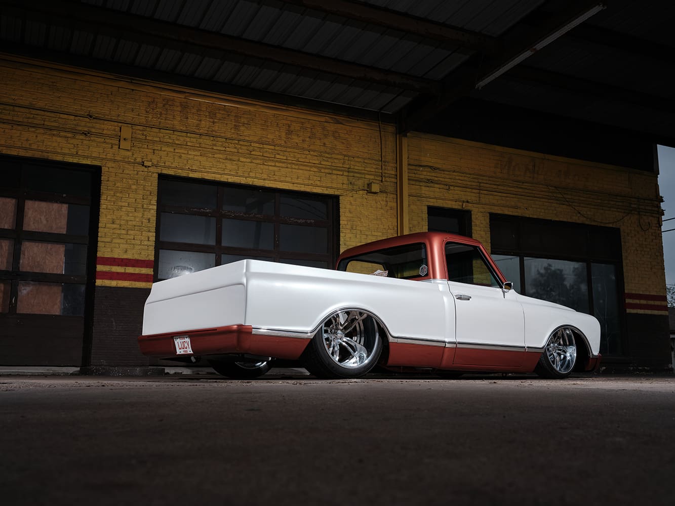 Low-angle view looking up at the rear quarter panel and deep-lip polished wheels of a bagged pearl white and copper 1968 Chevy C10 pickup.