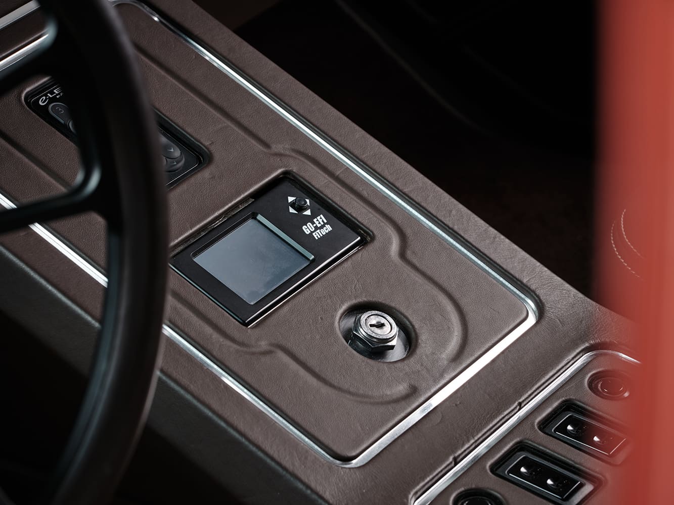 Close-up of the center console featuring an integrated FiTech Go-EFI touchscreen display, ignition switch, and rocker switches trimmed in stitched brown leather.