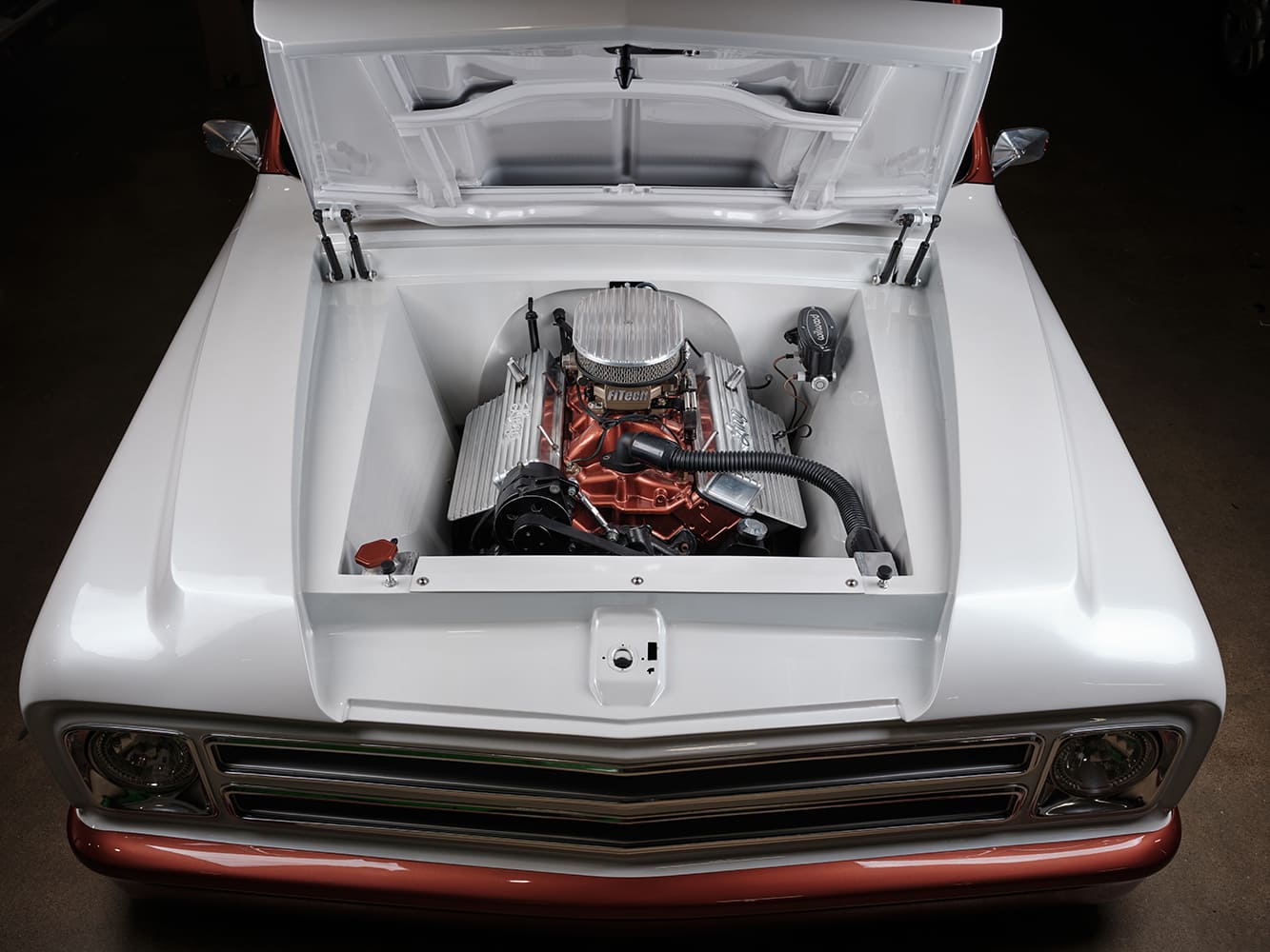 Front overhead shot of the shaved smooth white engine bay housing a copper-painted Chevrolet small-block V8 with finned valve covers and FiTech fuel injection.