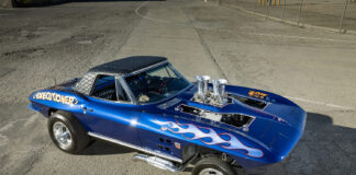 High-angle view of a blue 1964 Corvette gasser showing the diamond-stitched vinyl roof and dual velocity stacks through the hood.