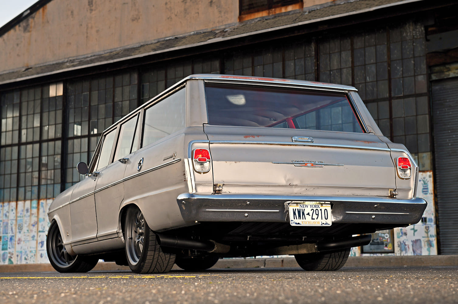 Low ground-level rear three-quarter view highlighting the tailgate, chrome bumper, New York license plate, and dual matte black exhaust tips under the chassis.