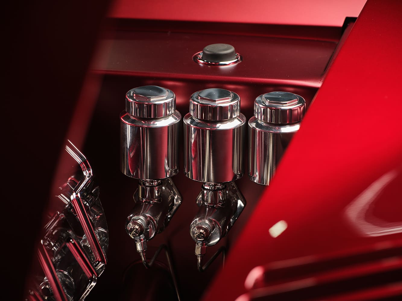 Macro close-up of three polished billet aluminum brake and clutch fluid reservoirs mounted neatly along the inner firewall cover.