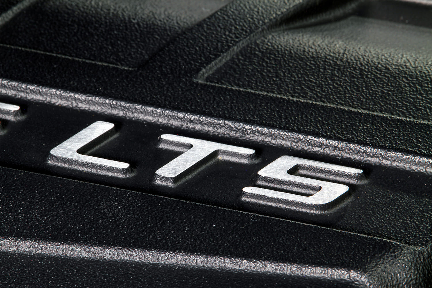 Macro detail of the machined LT5 logo emblem on the textured black supercharger lid.