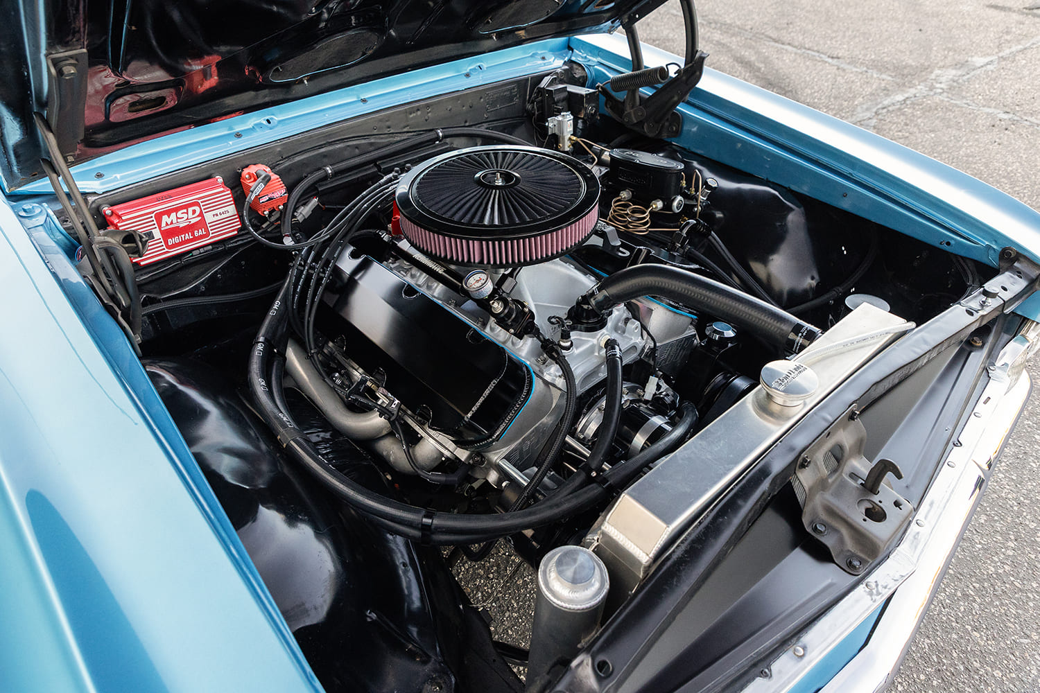 Wide engine bay shot showcasing a high-performance big-block Chevrolet V8 with gloss black valve covers, open element air cleaner, aluminum radiator, and MSD Digital 6AL ignition box.