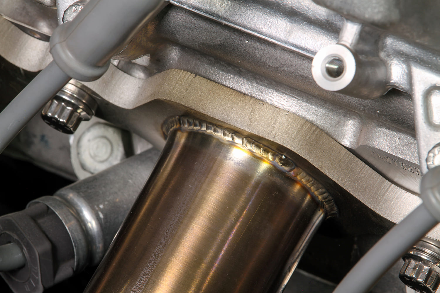 Close-up of a precision TIG-welded bead connecting a stainless steel exhaust header tube to the cylinder head flange.