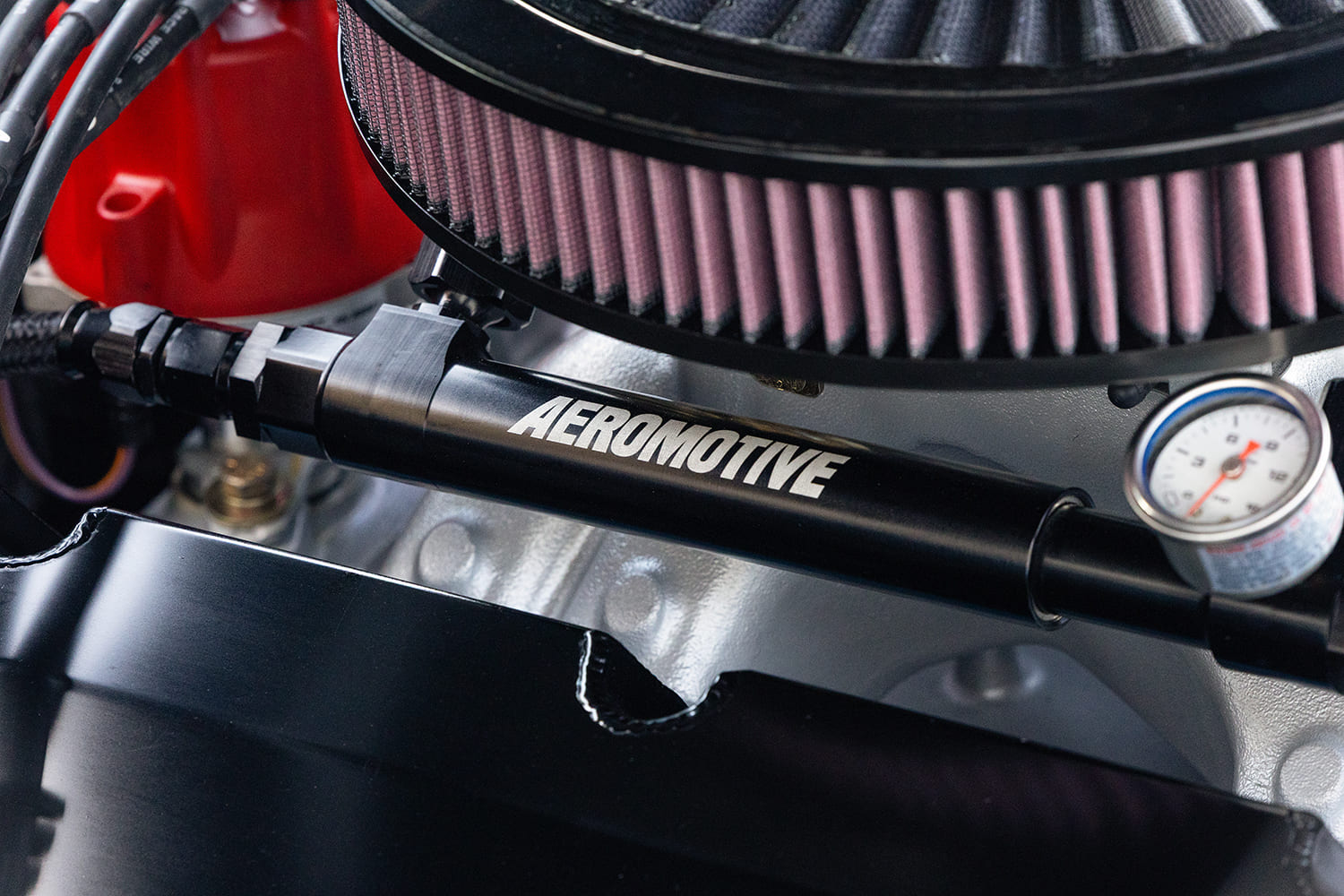 Macro close-up of a black anodized Aeromotive fuel log and mechanical pressure gauge mounted below the round performance air filter.