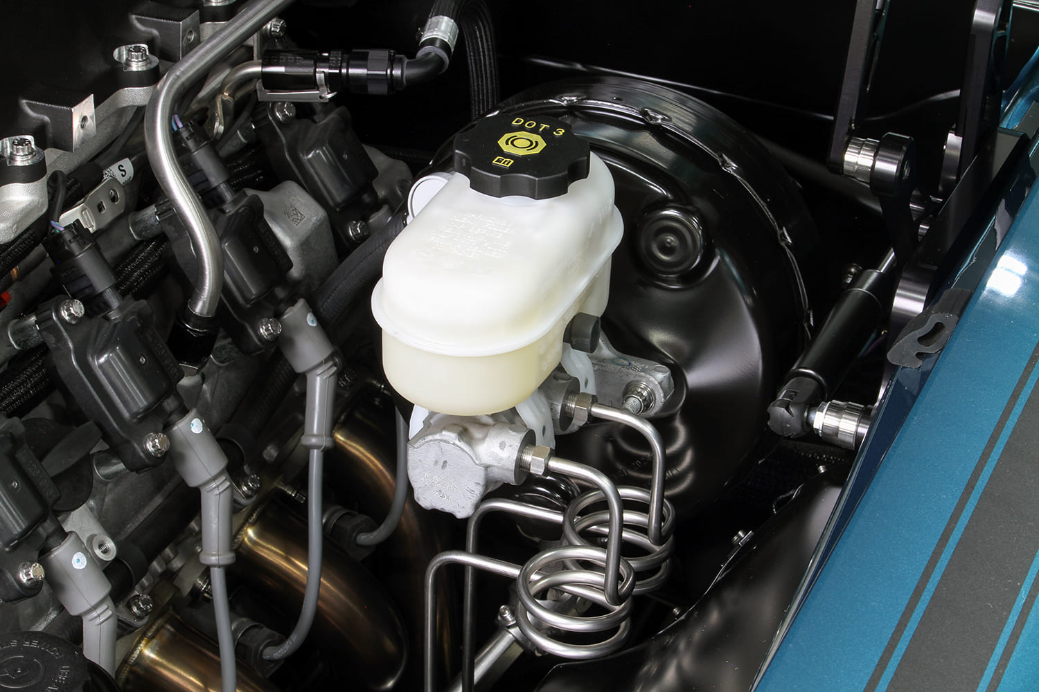 Modern black brake booster and clear master cylinder reservoir with coiled stainless brake lines in an engine bay.