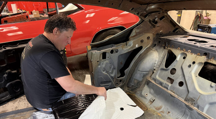 Installer test-fitting a precut Flatline Barriers insulation sheet over the rear floor pan in a stripped 1969 Chevelle interior.