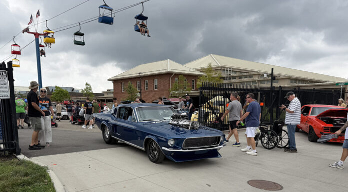 Dark blue 1967 Ford Mustang fastback with an exposed blower driving through the event gates under a ski lift at the Goodguys Columbus Nationals.