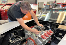 Mechanic lowering and test-fitting a FiTech Go EFI 4 throttle body onto an intake manifold in a 1971 Corvette engine bay.